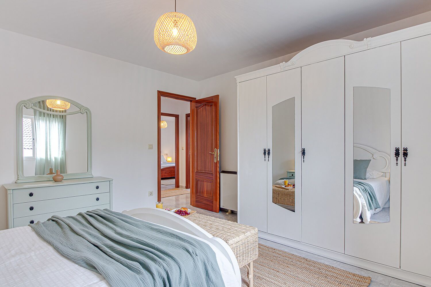 A bedroom with a bed, dresser, wardrobe, and a mirror.