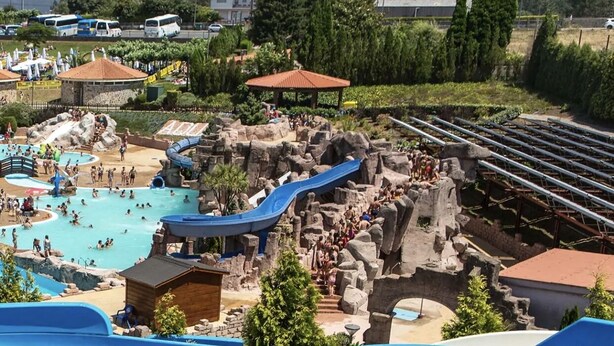 Ein Wasserpark mit mehreren Rutschen und Pools, umgeben von felsigem Gelände und Bäumen.