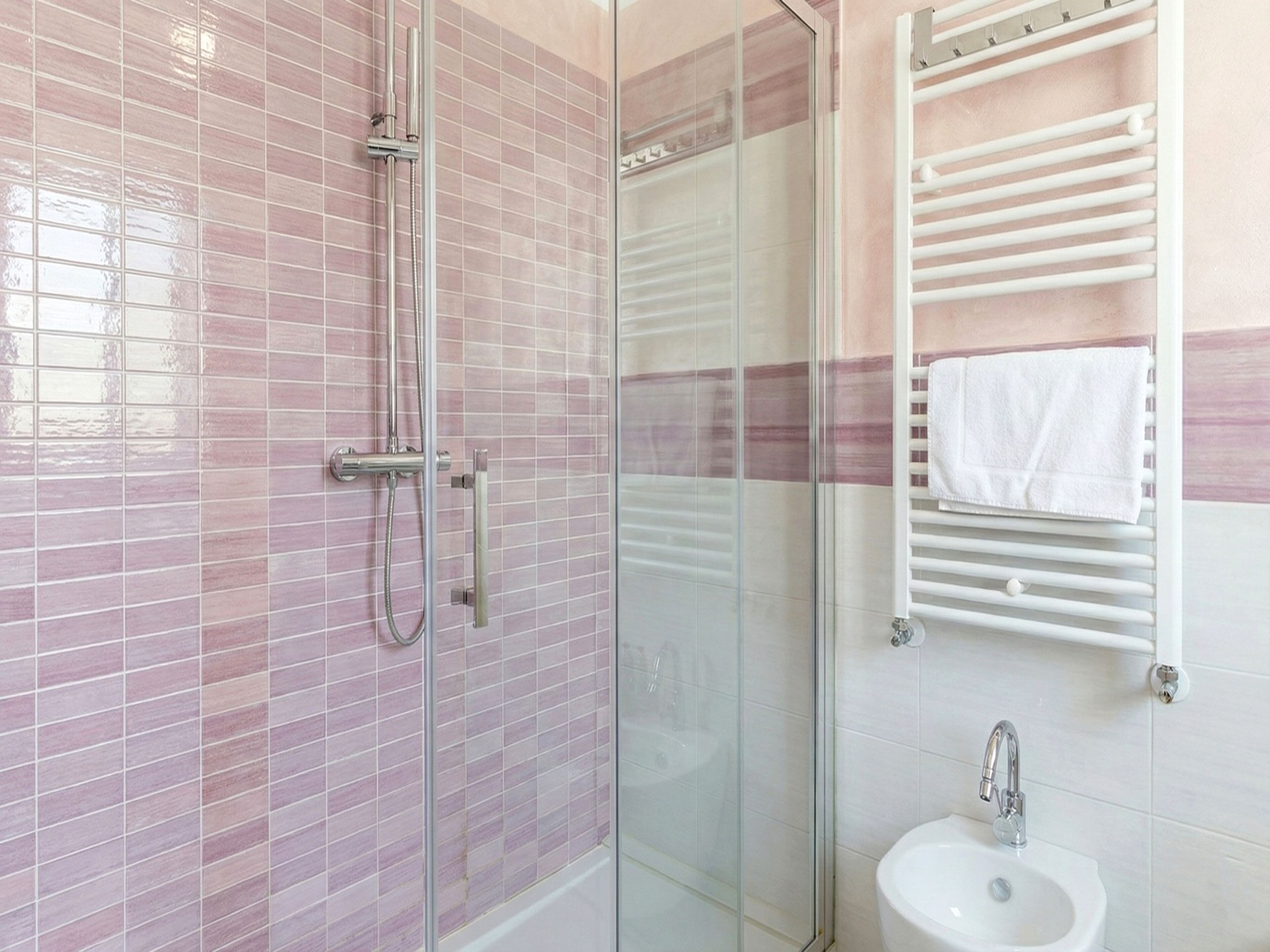 A bathroom with a glass shower enclosure, a white sink, and a towel rack.