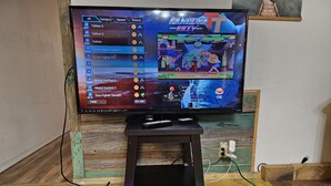 Un televisor mostrando un videojuego, conectado a una consola de juegos sobre un pedestal de madera.