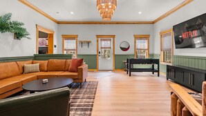 Un salon spacieux doté d’un plancher en bois, d’un canapé en cuir marron, d’une table basse, d’une table de billard et d’un téléviseur fixé au mur.