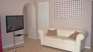 Uma sala de estar moderna com uma televisão de tela plana, um sofá branco e uma obra de arte colorida na parede.