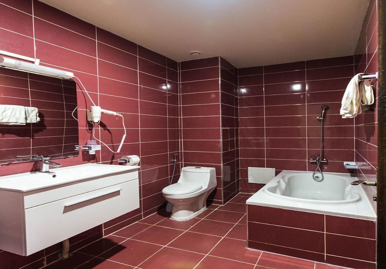 Une salle de bain moderne avec un lavabo, des toilettes et une baignoire, le tout mis en valeur par un mur recouvert de carreaux rouges.
