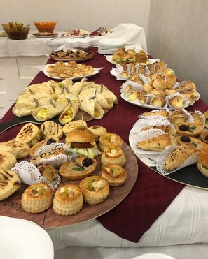 Uma mesa de buffet com diversos alimentos, incluindo pastelaria, sanduíches e sobremesas.