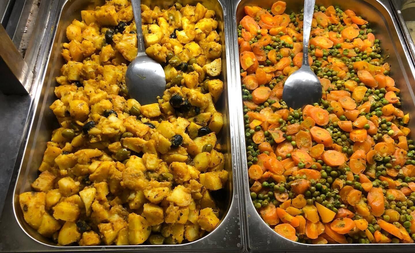 Two buffet trays with various vegetables and a spoon in each.