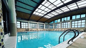 An indoor swimming pool with clear glass ceilings, tiled walls, and lounge chairs around the pool. - Syphax Tichy Plage (Tichy)