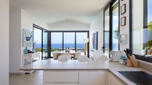 Una cocina moderna con una isla grande, un comedor con vista al mar y una mesa para cuatro.
