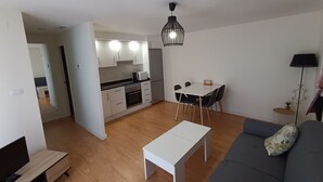 Uma sala de estar moderna com um sofá, uma mesa de jantar e uma cozinha ao fundo.