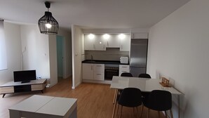 Uma cozinha moderna com armários brancos, uma geladeira de aço inoxidável e uma área de jantar com mesa e cadeiras.