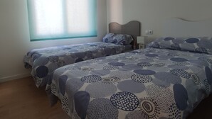Quarto de hotel com duas camas, uma janela com persianas, mesa de cabeceira e tomada na parede.