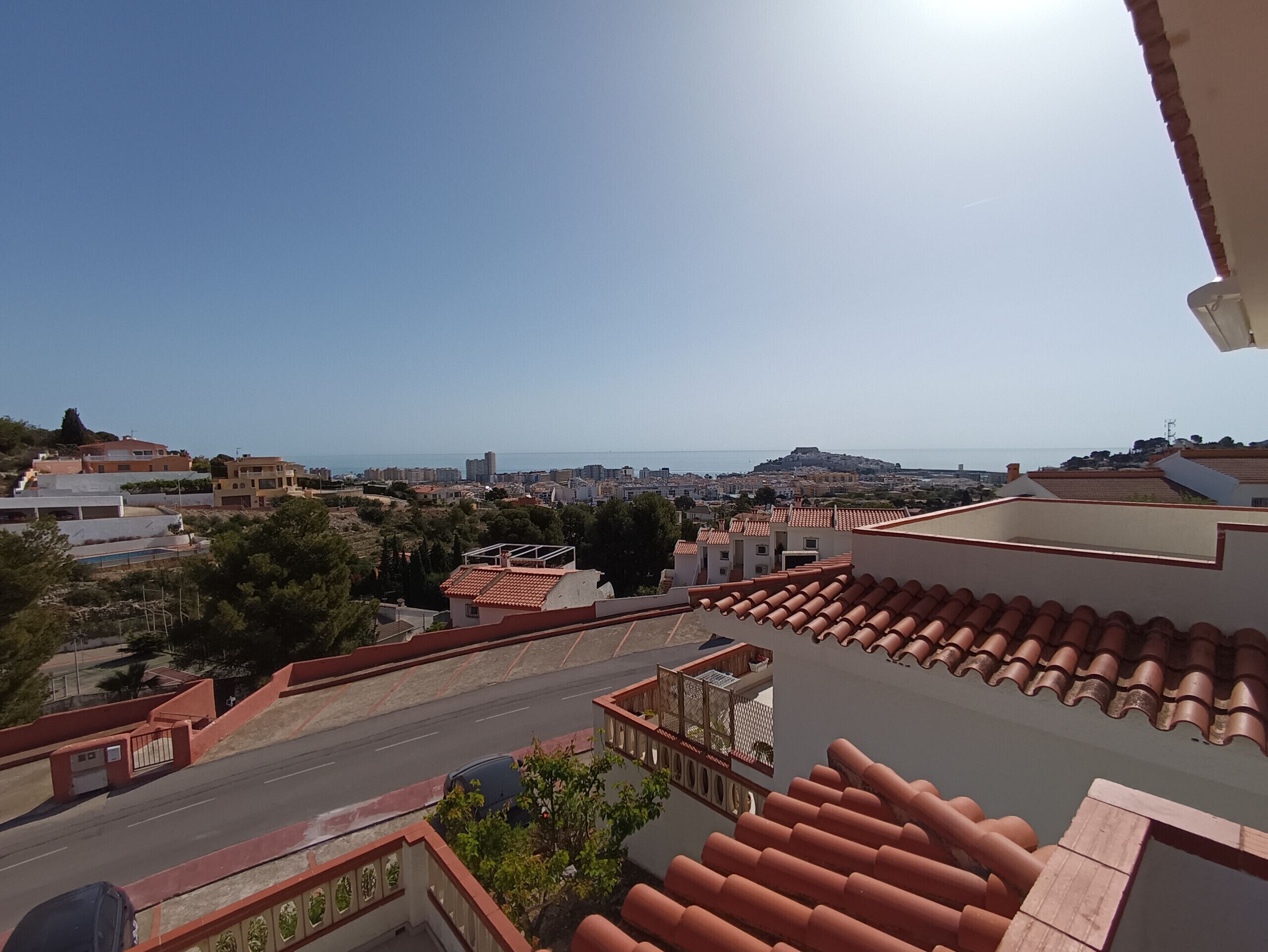 A residential area with terracotta-tiled roofs, a street, and a distant view of a hill with buildings.
