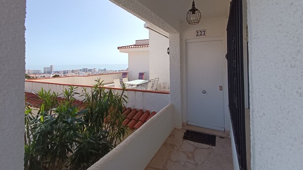Varanda com vista para a cidade, uma porta com o número 227 e um lustre pendente.