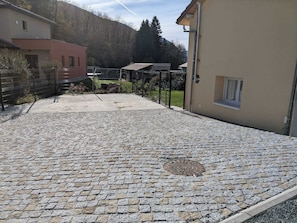 A paved courtyard with cobblestone flooring, surrounded by buildings and a mountain backdrop. - Maison Individuelle 2 Chambres six Couchages au Centre Village (Vaulnaveys-le-Haut)