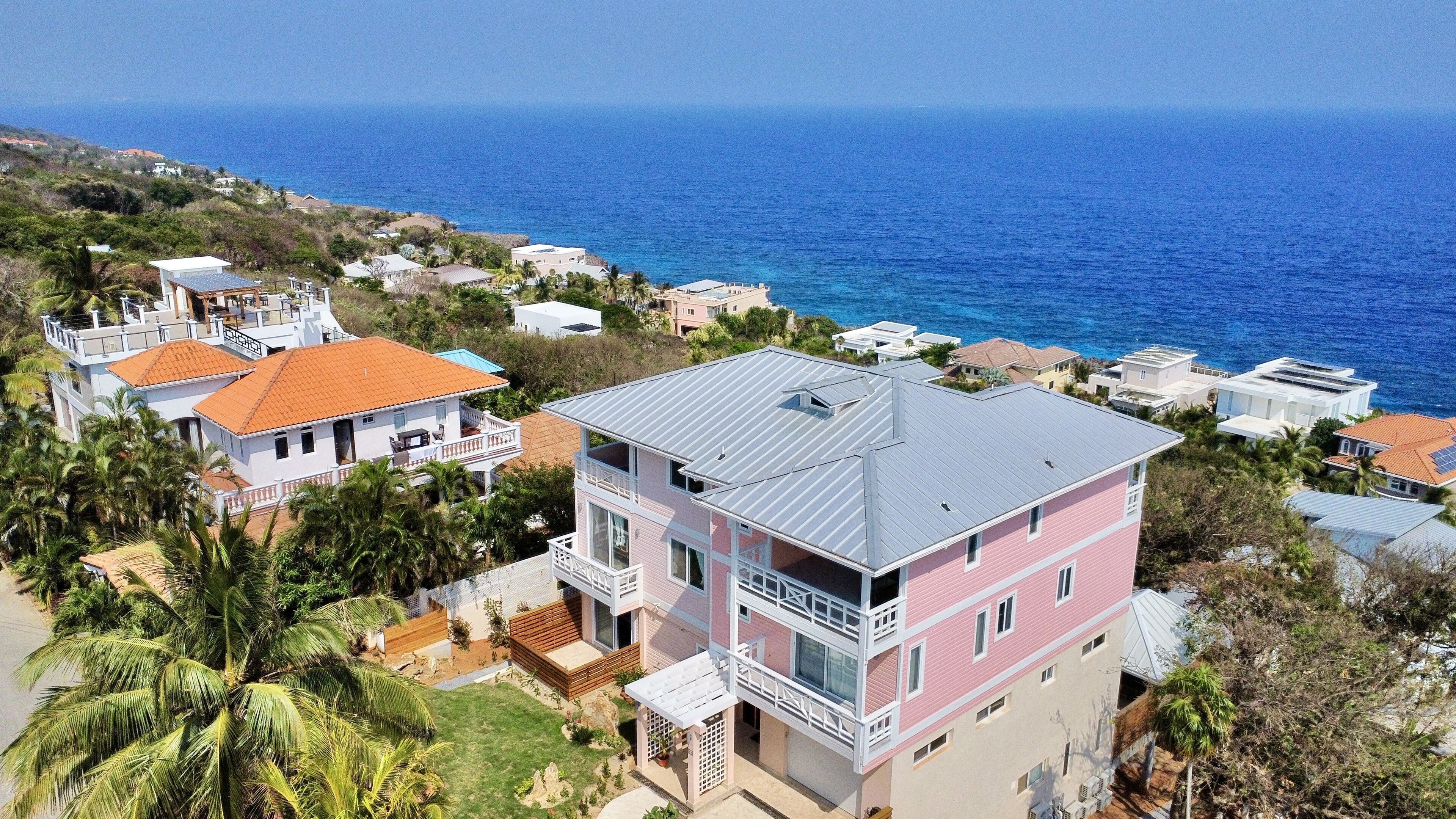 A multi-story building with a flat roof, surrounded by palm trees and a view of the ocean.