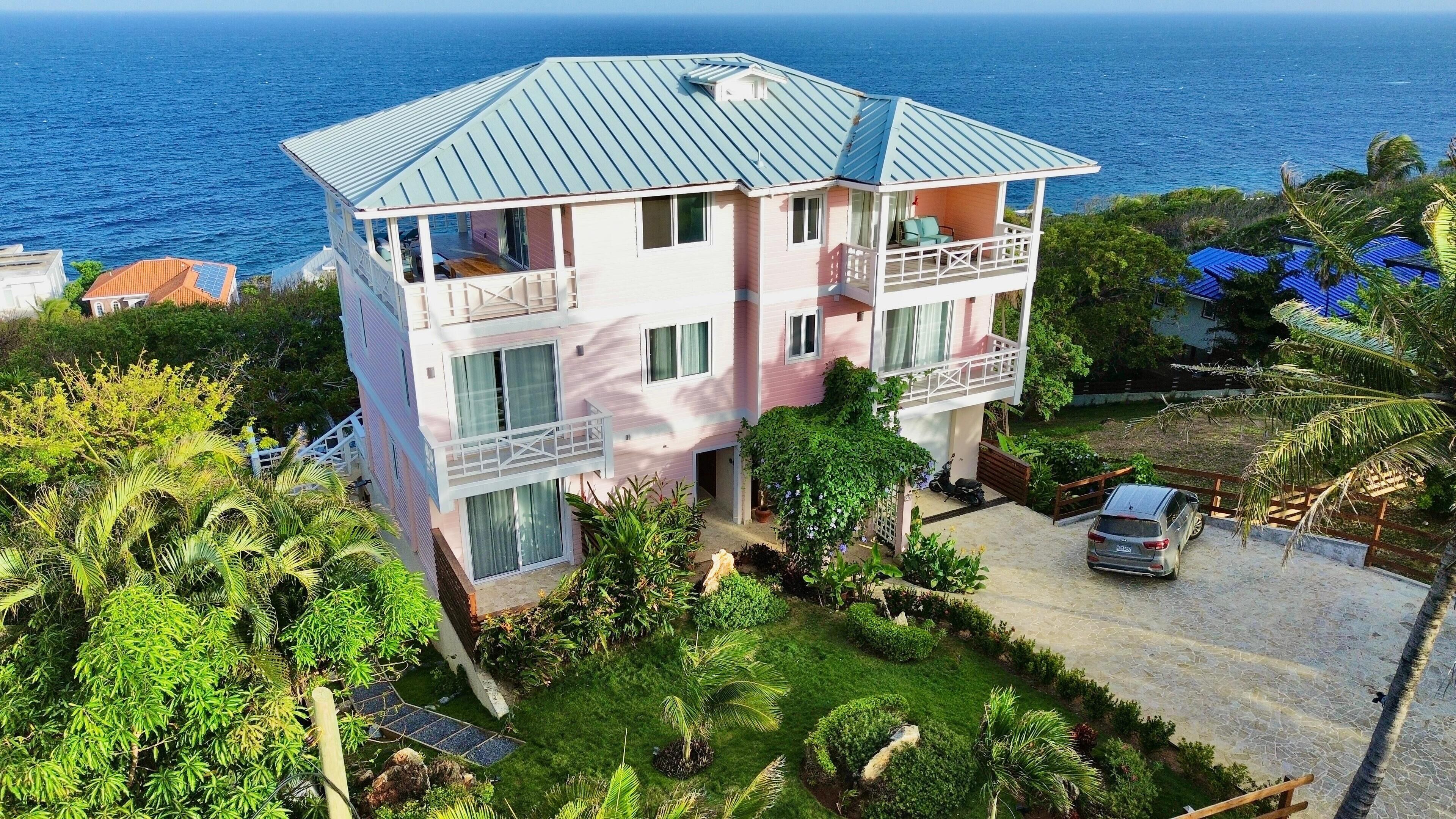 Un edificio de varios pisos con balcón, rodeado de vegetación exuberante y vistas al mar.