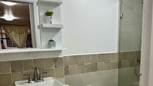 A bathroom with a sink, toilet, and shower. There are shelves with plants and a trash bin.