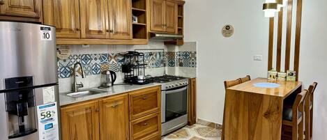 A kitchen with wooden cabinets, a stainless steel refrigerator, a gas stove, and a dining table with chairs.