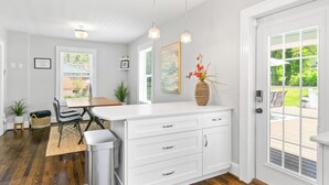 Een keuken met witte kasten, een houten eettafel en hanglampen.