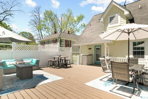 Une terrasse en bois avec des meubles d’extérieur, notamment une table et des chaises, et un patio couvert doté d’un parasol.