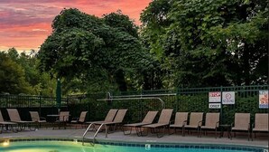 A swimming pool with lounge chairs and safety signs, surrounded by trees.