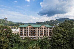 A multi-story hotel with a green roof, surrounded by trees and hills.