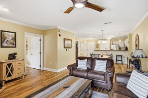 A spacious living room with a brown leather sofa, a wooden coffee table, and a dining area in the background.