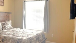 Ein Schlafzimmer mit einem Bett, einem Deckenventilator, einem Fenster mit Vorhängen und Holzdielen.