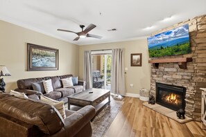Una sala de estar con chimenea de piedra, sofás de cuero, televisor de pantalla plana y ventilador de techo.