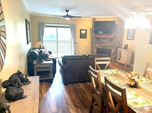 Ein Wohnzimmer mit Kamin, einer Couch, einem Esstisch mit Stühlen und einem an der Wand befestigten Fernseher.