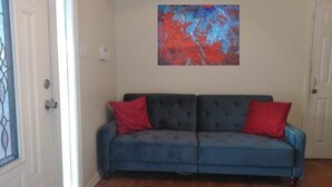 Un sofá azul con cojines rojos, una alfombra colorida y un cuadro abstracto rojo en la pared.
