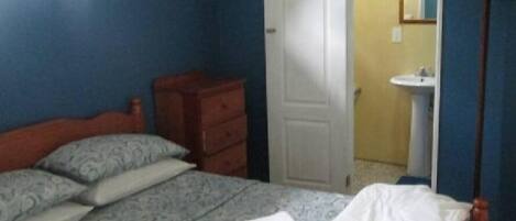 Une chambre à coucher comprenant un lit, une commode, une porte donnant sur une salle de bain et un miroir au mur.