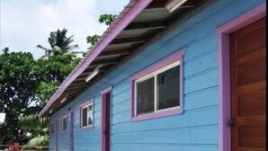 Un edificio de dos pisos con fachada azul y detalles en rosa. Se observan dos ventanas en la planta baja y una puerta a la derecha.