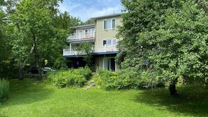 A two-story house with a backyard featuring a fire pit and a wooden bench. - Charming Home, Panoramic Mountain Views, Ideal For Family (Bolton-Ouest)
