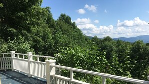 A wooden deck with white railings overlooking a dense forest and distant mountains. - Charming Home, Panoramic Mountain Views, Ideal For Family (Bolton-Ouest)