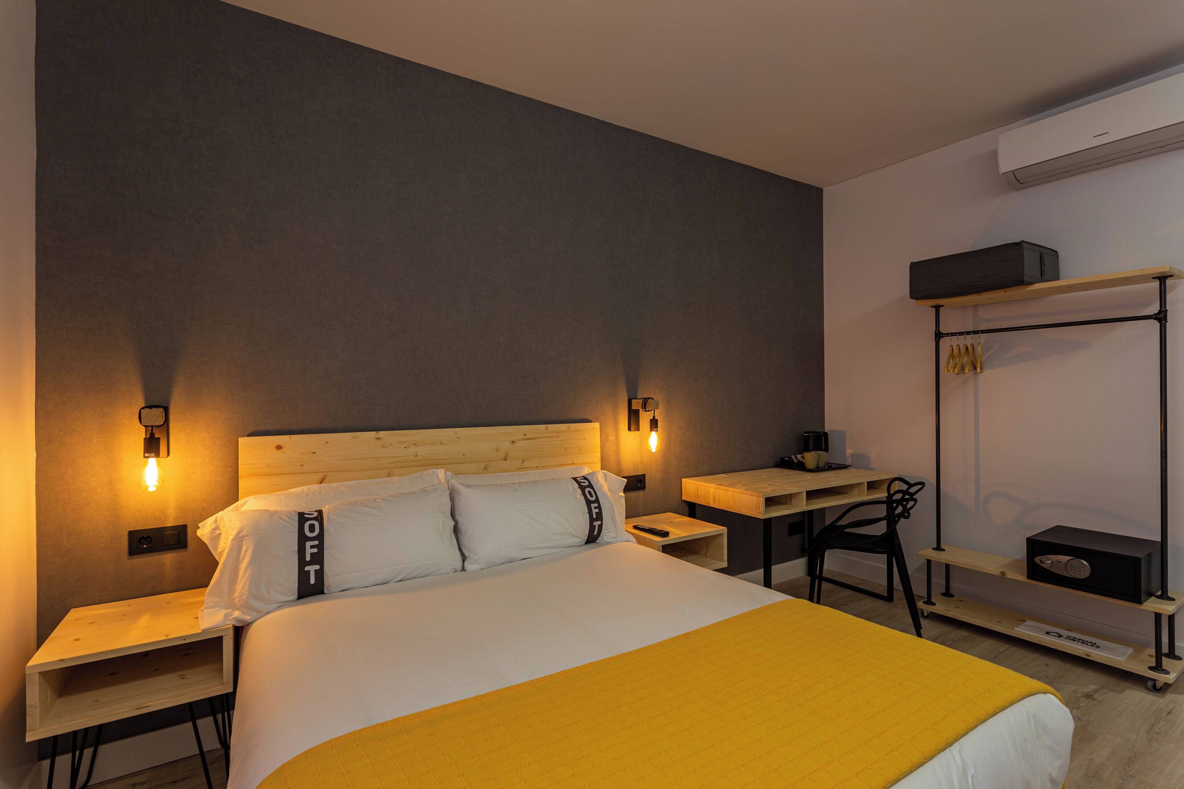 Una habitación de hotel con cama, mesitas de noche, escritorio, silla y un perchero en la pared.