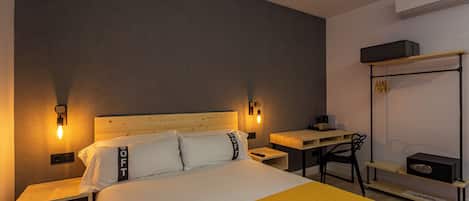 Una habitación de hotel con cama, mesitas de noche, escritorio, silla y un perchero en la pared.