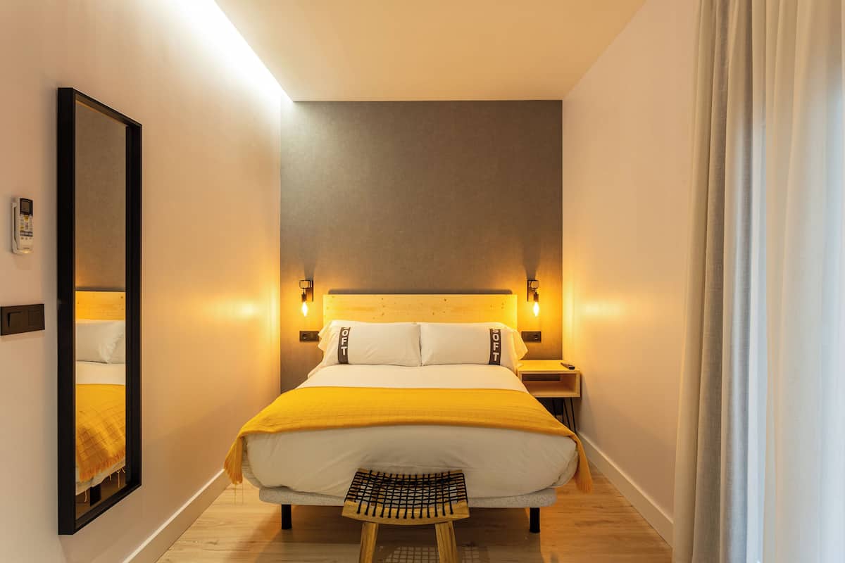 A hotel room with a large bed, bedside tables, a mirror, and a wooden floor.