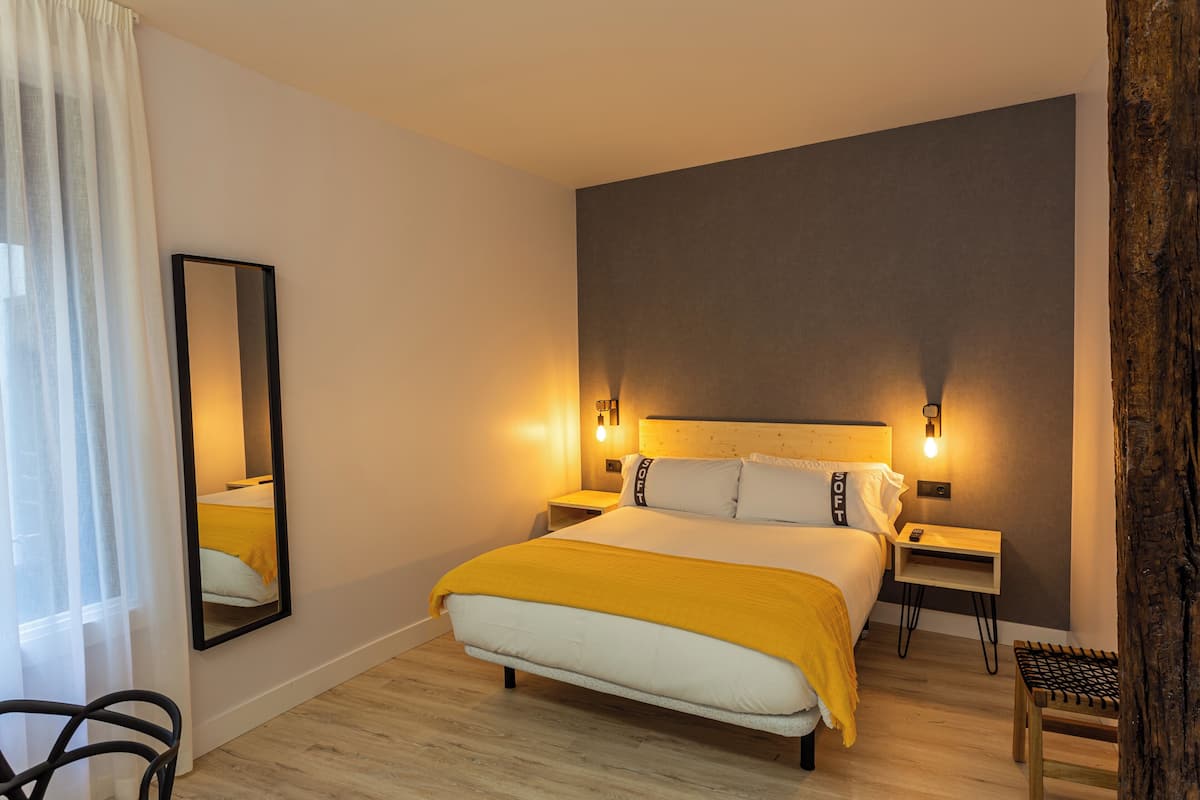 A hotel room with a large bed, bedside tables, a mirror, and a view of the outdoors.