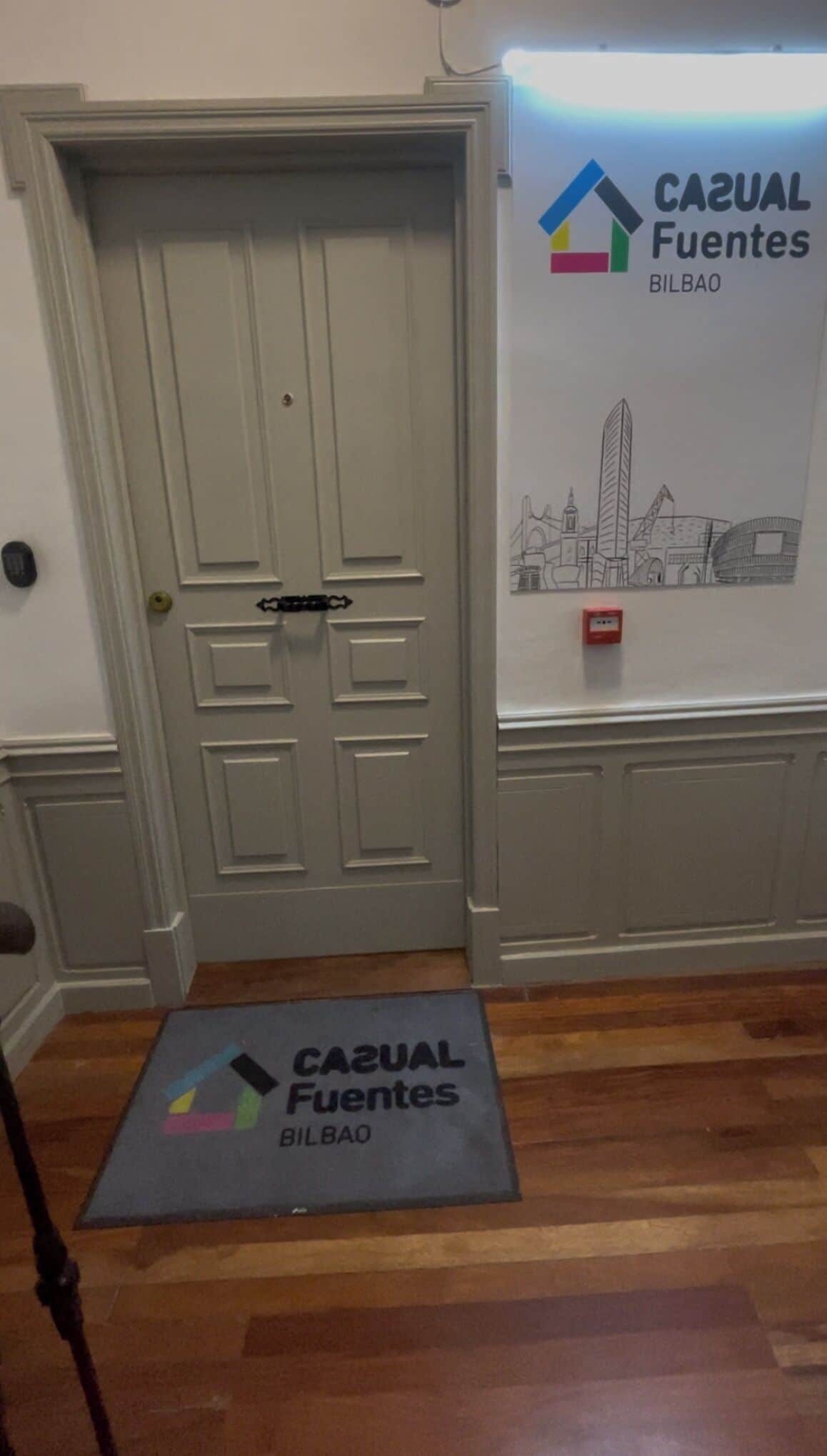 A door with a doorknob and a mat with the logo "Casual Fuentes Bilbao" on the floor.