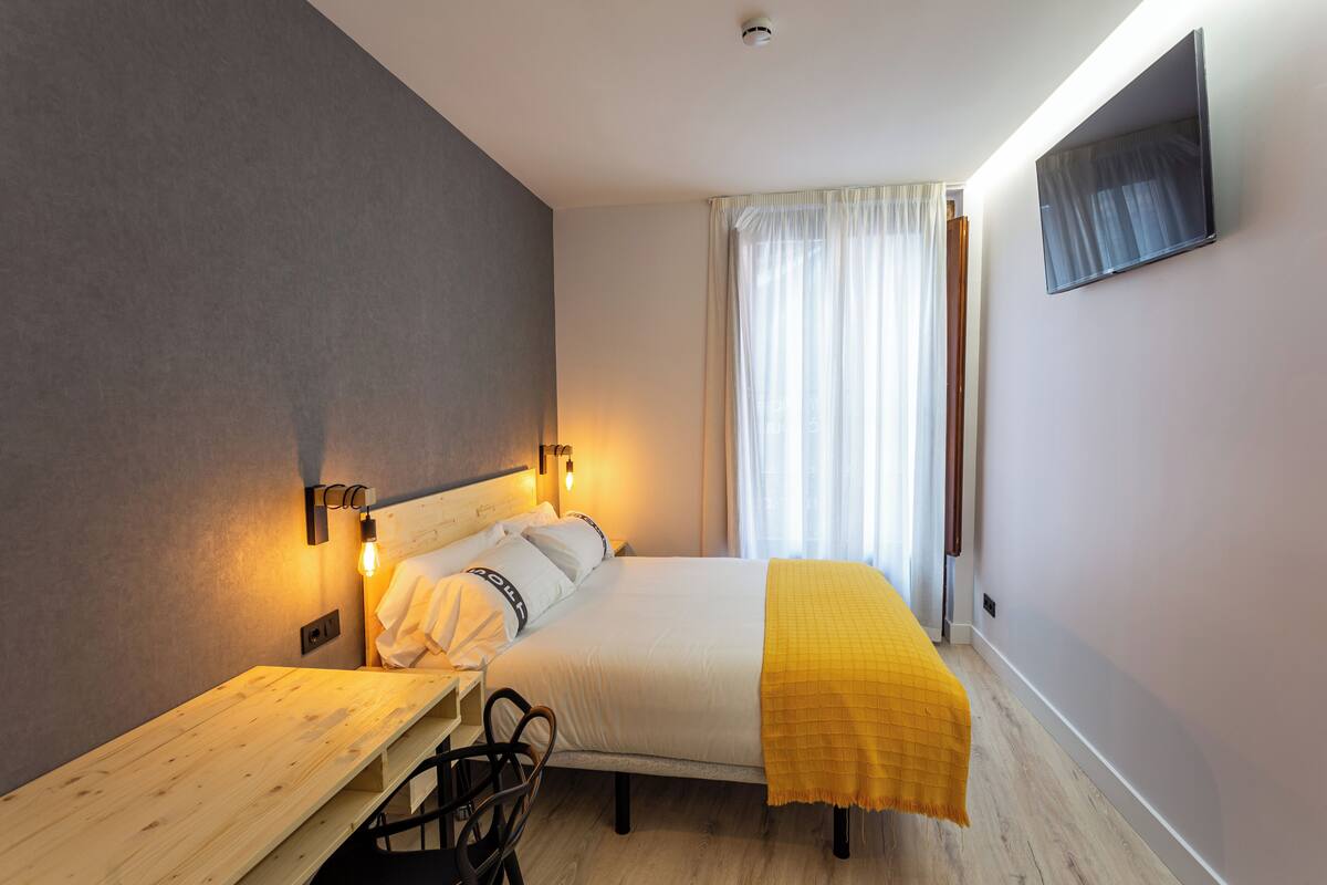 A bedroom with a bed, bedside table, lamp, and a TV mounted on the wall.