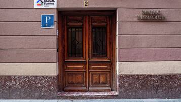 L'ingresso di un edificio con una porta in legno a due ante, un segnale di parcheggio e una targa con su scritto "Francisco de la Roca de Chea".