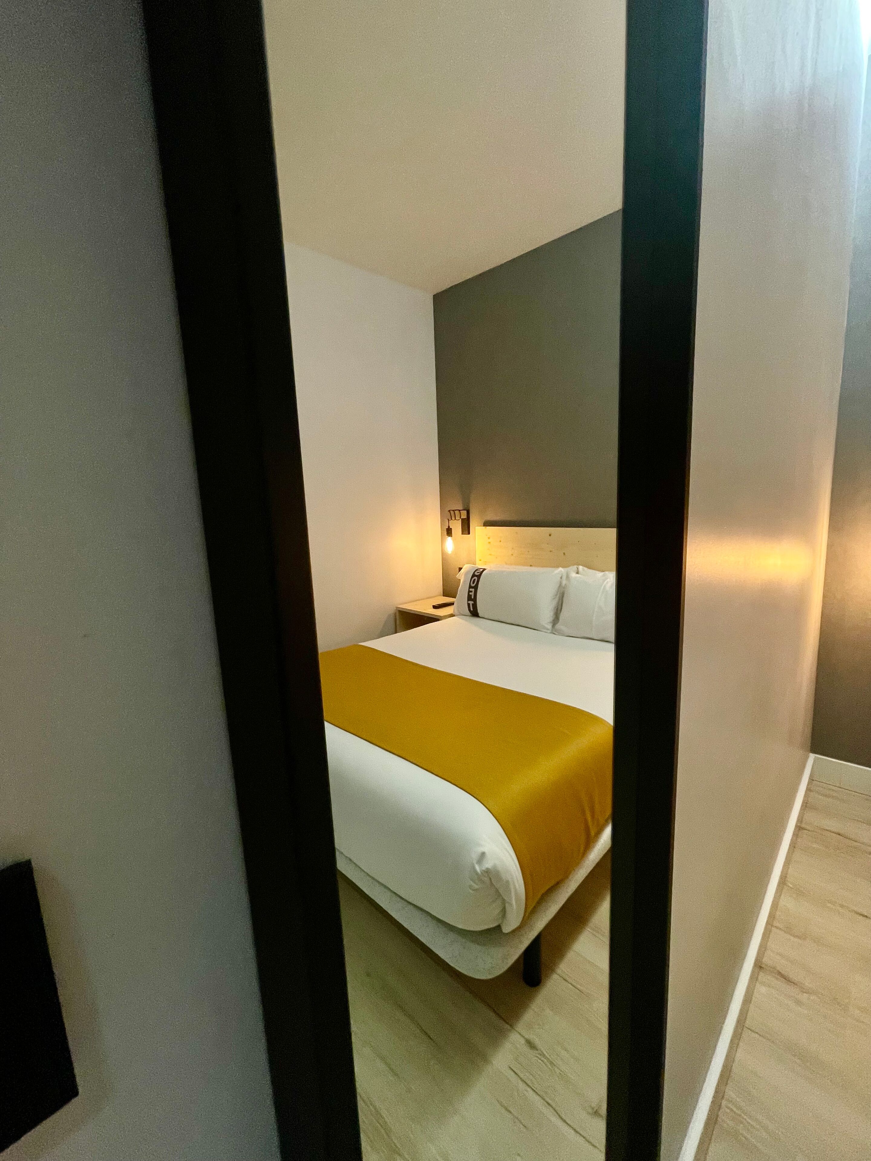 Een moderne hotelkamer met een bed, nachtkastje en een wandlamp.