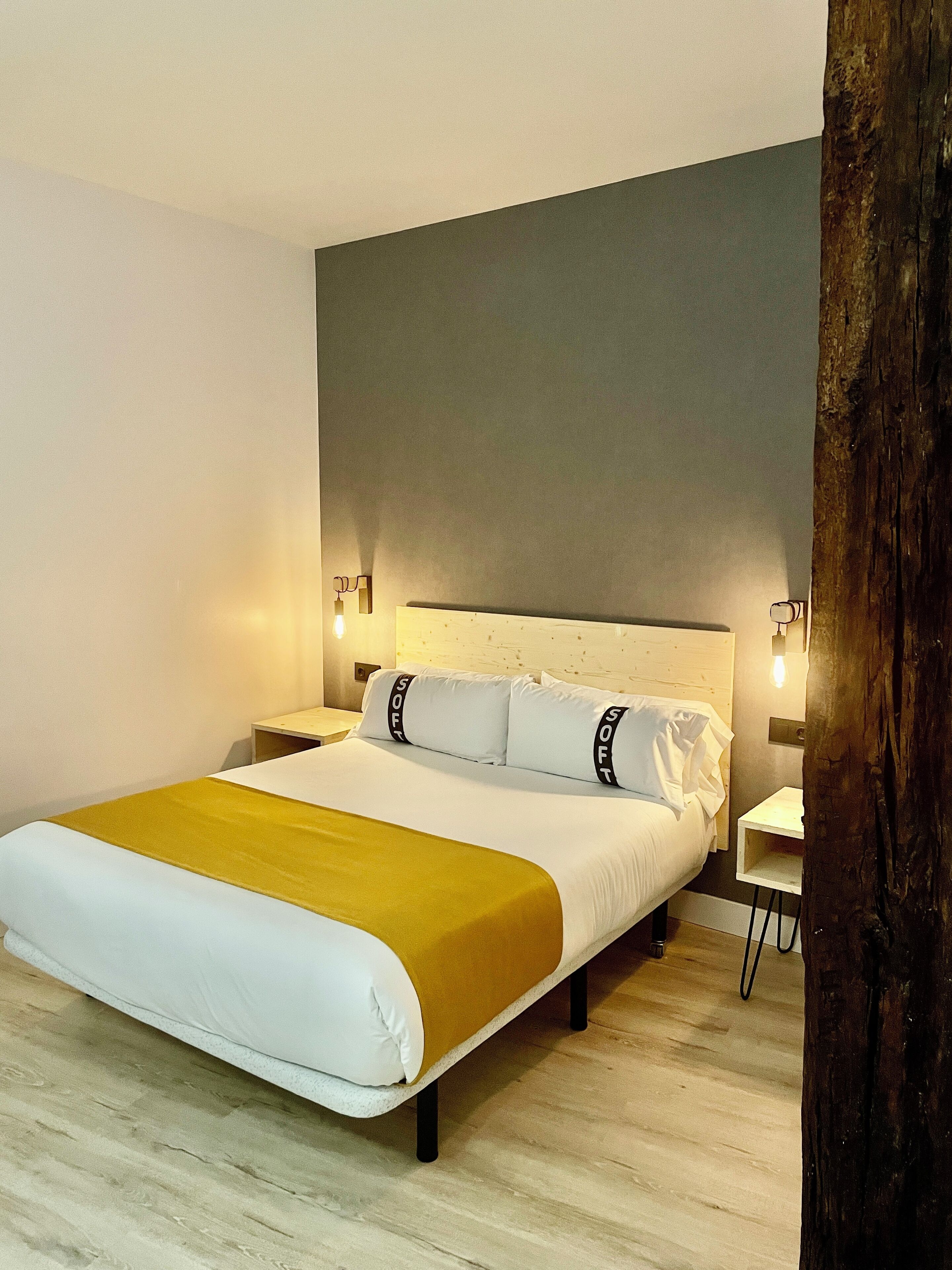 A modern hotel room with a large bed, a wooden floor, and a grey accent wall.