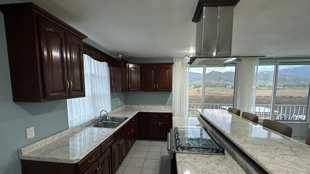 Cozinha com armários de madeira escura, bancada de mármore e uma grande janela com vista para uma paisagem deslumbrante.