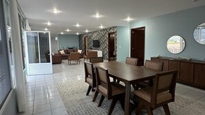Uma ampla área de refeições com uma grande mesa de madeira e cadeiras, um conjunto de sofás e uma parede com padrão losango.