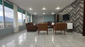 Um quarto espaçoso com grandes janelas, parede com padrão losango e televisão de tela plana.