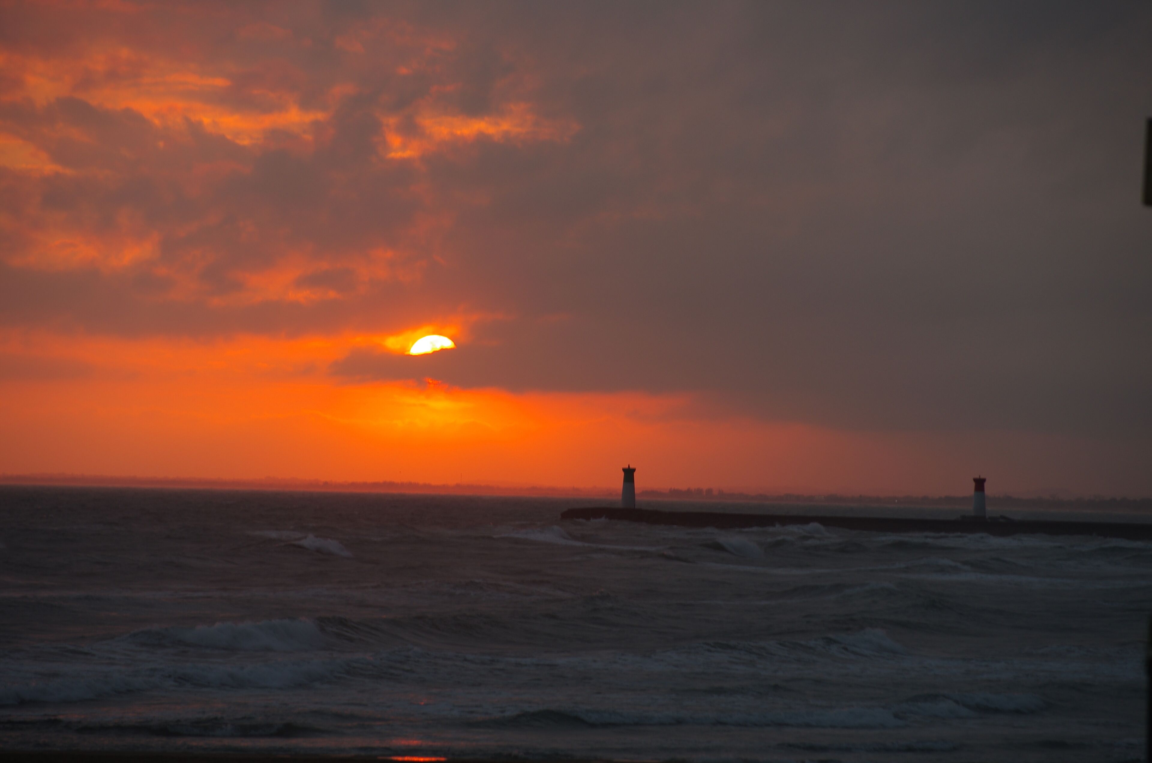 Un coucher de soleil sur l’océan, avec un phare qui se dessine à l’horizon.