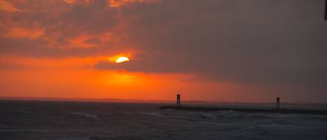 Un coucher de soleil sur l’océan, avec un phare qui se dessine à l’horizon.