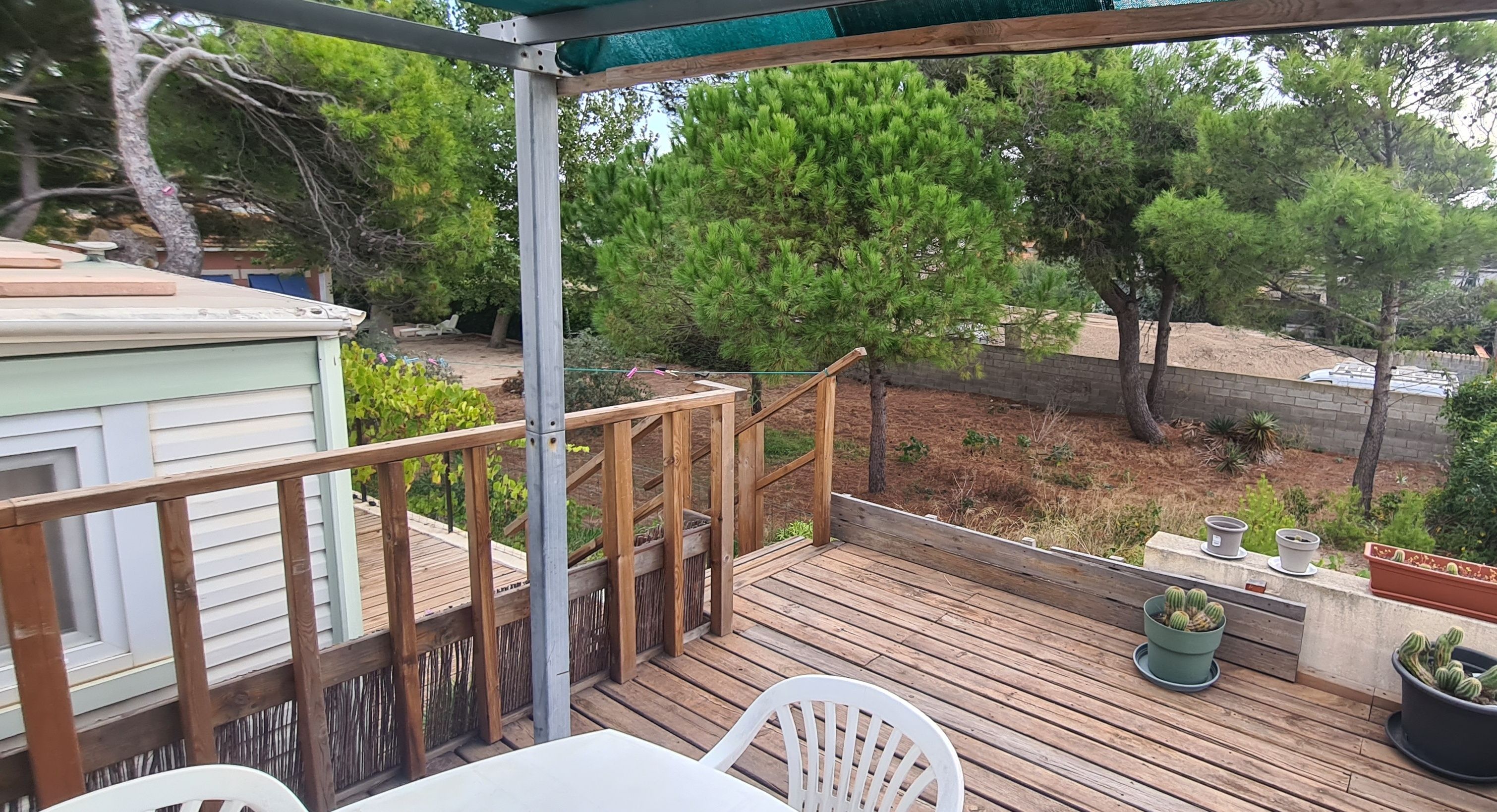 A wooden deck with a table and chairs, surrounded by a wooden fence and a green pergola.