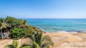 Una playa con agua cristalina, palmeras y un litoral rocoso.